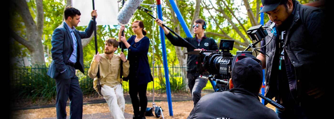 Three NYFA AU filmmaking students talk by a swingset while being filmed by a RED Camera.